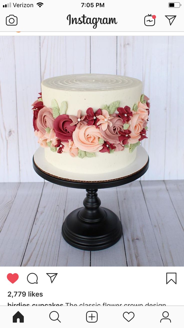 a white cake with pink and red flowers on it sitting on top of a wooden table