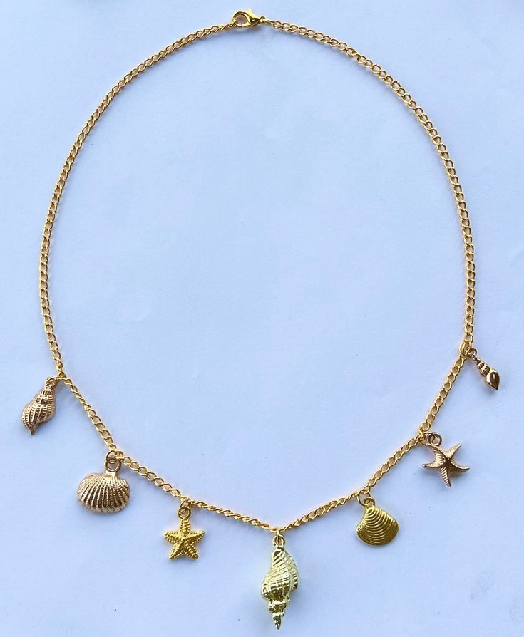 Introducing the cutest Dainty Gold Conch Shell Charm Necklace, adorned with an array of exquisite beach-inspired charms. This stunning piece uses a simple gold chain to captures the essence of the ocean, bringing a touch of elegance and sophistication to any ensemble.  The centerpiece of this necklace is a radiant gold conch shell, symbolizing tranquility, beauty, and the serenity of the coast. Adorning either side of the conch are intricately designed gold starfish, gold clam shells, and gold s Cheap Starfish Charm Jewelry For Vacation, Dainty Beach Necklace With Delicate Chain, Dainty Necklace With Delicate Chain For Beach, Dainty Beach Jewelry With Delicate Chain, Ocean-inspired Jewelry With Lobster Clasp For Vacation, Dainty Gold Starfish Charm Necklace, Dainty Strand Jewelry For The Beach, Gold Ocean-inspired Jewelry With Dangling Charms, Beach Jewelry With Charms In Ocean-inspired Style