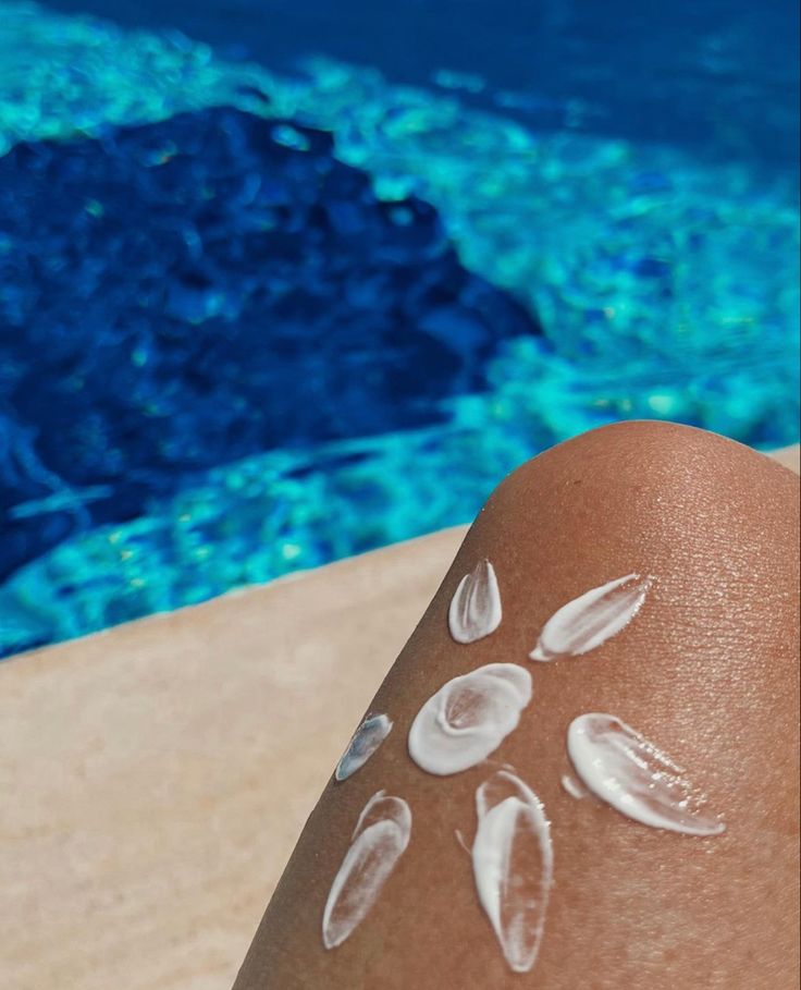 a person's legs with white paint on them next to a swimming pool and blue water