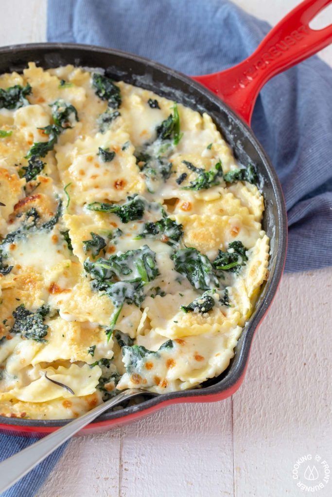 a red skillet filled with cheese and spinach on top of a blue towel