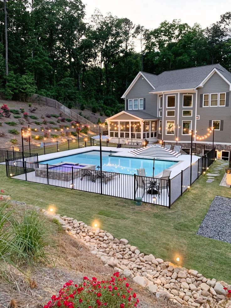 an aerial view of a backyard with a pool and deck lighting at night, surrounded by landscaping