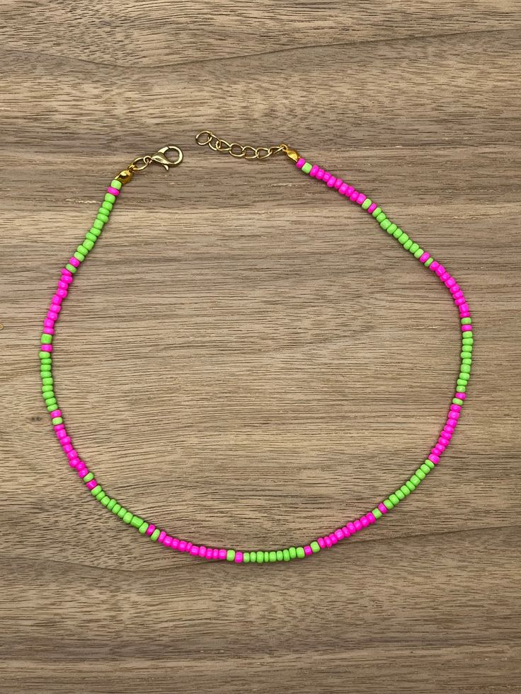 a pink, green and yellow beaded necklace on a wooden surface with a gold chain