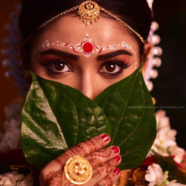 a woman with her face painted in gold and holding a green leaf to her face