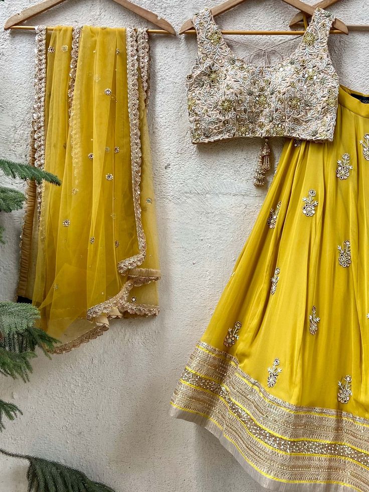 A three-piece mustard and beige mirror lehenga set from the Priti Sahni collection. This mustard georgette floral mirror embroidery butti lehenga with a heavy border of zari-pearl work detail is paired with a raw silk beige cutwork blouse with mirror, zardozi, resham work all over it. This outfit is completed with a mustard tulle net dupatta with scallop edging with highlights. Transitional Gold Pre-draped Saree With Gota Work, Transitional Chanderi Lehenga With Gota Work, Floor-length Pre-draped Saree With Gota Work For Festivals, Yellow Pre-draped Saree For Transitional Wedding Season, Transitional Season Gold Lehenga With Gota Work, Transitional Gold Lehenga With Gota Work, Transitional Gold Lehenga With Cutdana, Pre-draped Anarkali Saree With Gota Work, Eid Lehenga With Mirror Work In Chinon