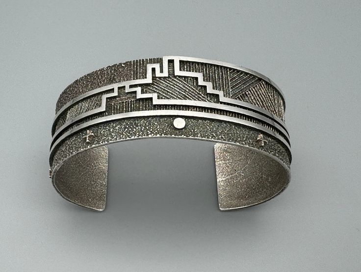 a silver cuff with an intricate design on the outside and inside, sitting on a gray surface