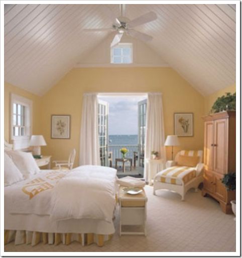 a bedroom with yellow walls and white bedding has a large window overlooking the ocean