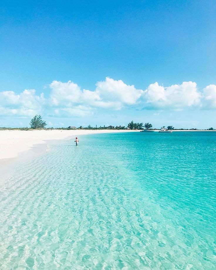 a person standing in the water on a beach with clear blue water and white sand