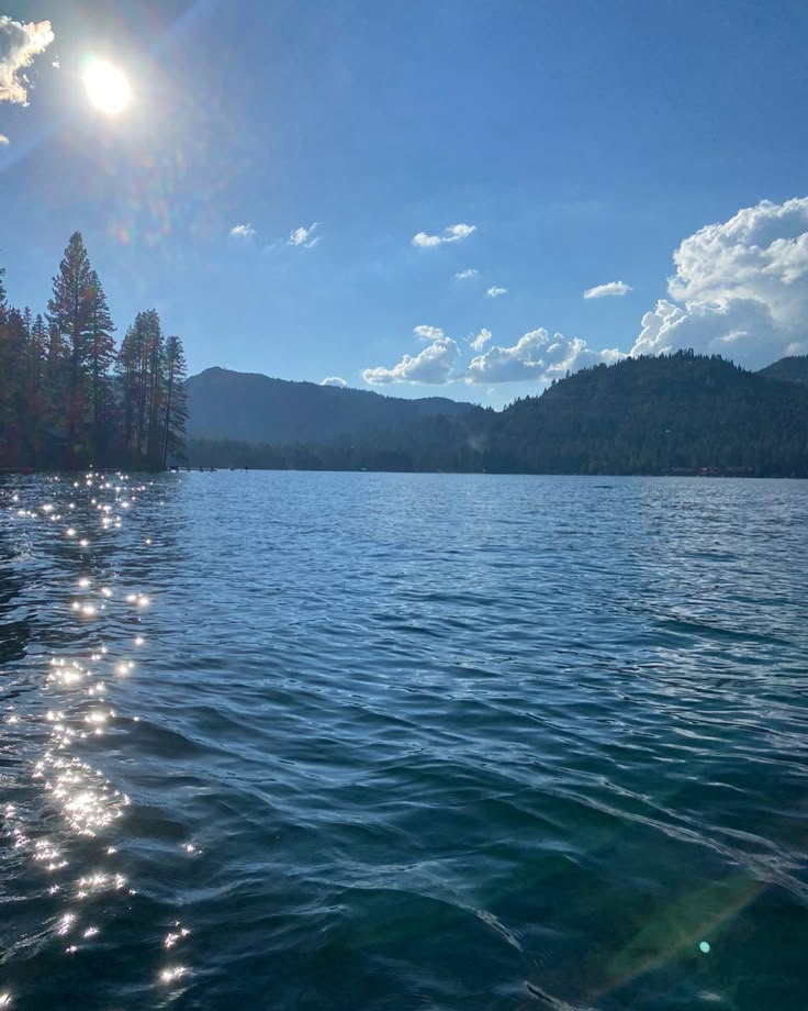 the sun shines brightly over water with trees in the background