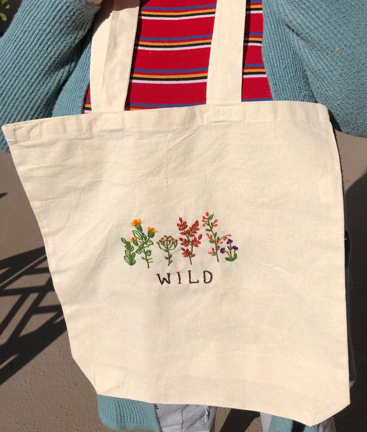 a woman carrying a white bag with wild embroidered on it's front and side