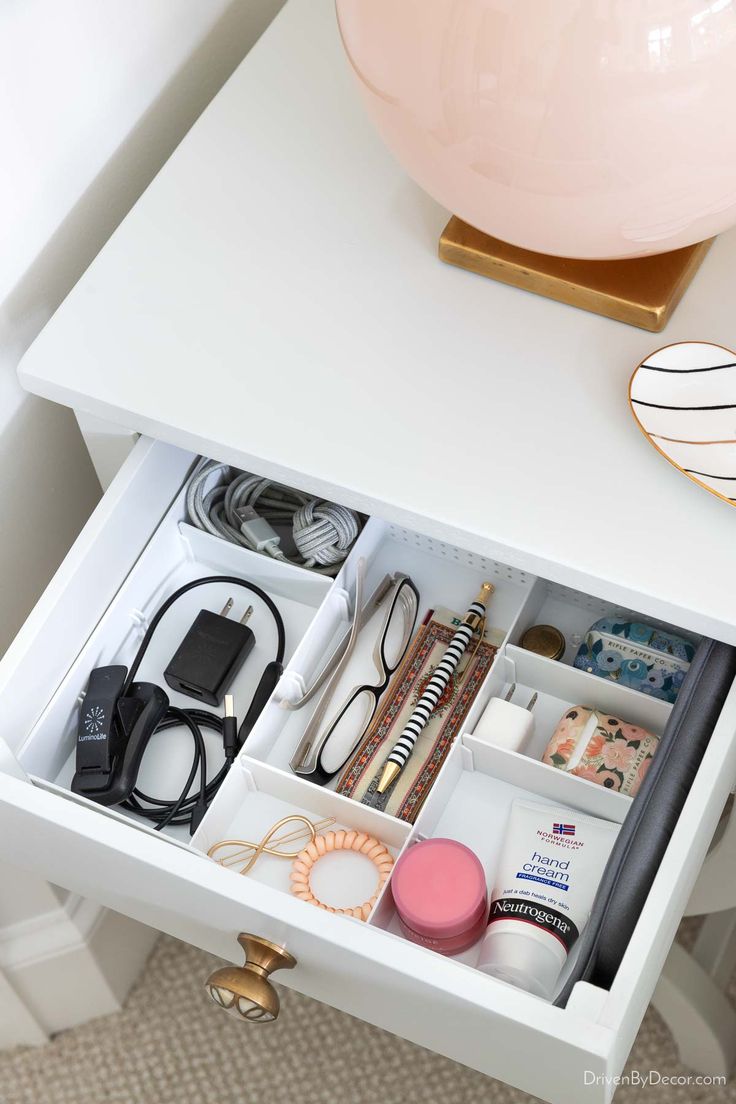 an open drawer in a white cabinet filled with cosmetics and other personal care items next to a pink lamp