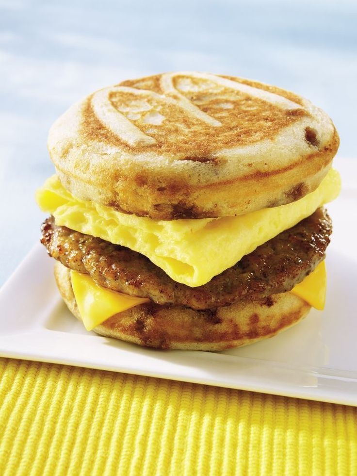 a breakfast sandwich with eggs and sausage is on a white plate next to a yellow place mat