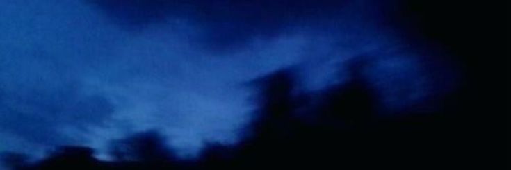 an airplane flying in the sky at night with dark clouds behind it and blue hues