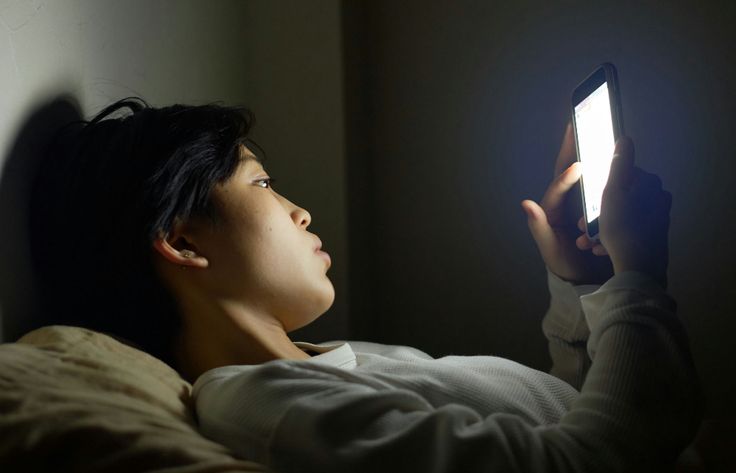 a woman laying in bed looking at her cell phone with the light shining on her face