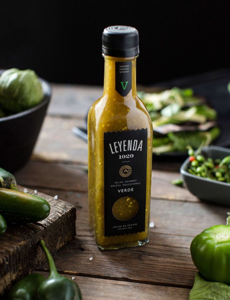 a bottle of yellow sauce sitting on top of a wooden table next to green peppers