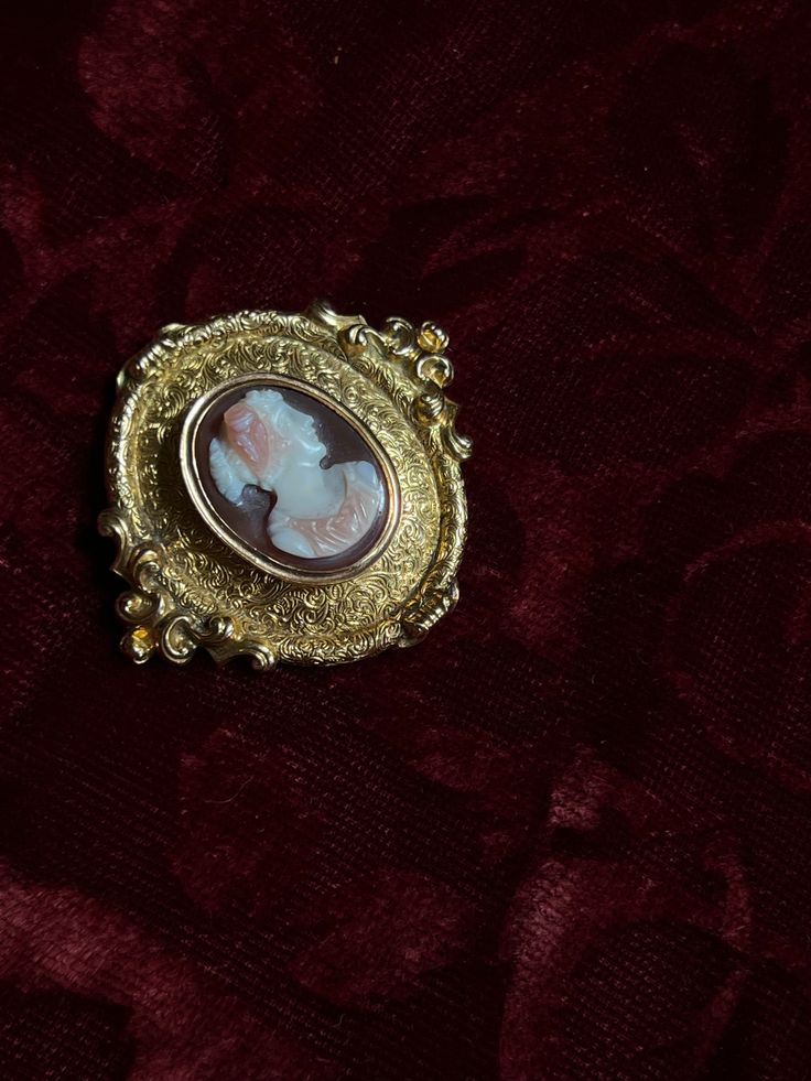 An adornment worthy of a museum! This stunning 19th century Sardonyx Cameo is a testament to Napoleon era French jewelry design. Crafted circa 1850-1860 in 18 carat gold, this brooch features a vibrant cameo of a aristocratic woman, set again a delicate peachy-hued sardonyx mount. The 18-carat gold mounting is also exceptional, with a gilded design brimming with fine detailing, and scrolling foliate motifs. The silhouette it creates makes it feel as if it should be hung in the halls of a palace! Elegant Yellow Gold Baroque Brooches, Luxury Oval Cabochon Brooches, Antique Yellow Gold Brooches With Intricate Design, Yellow Gold Baroque Brooch For Formal Occasions, Antique Gold Jewelry For Opera, Formal Yellow Gold Baroque Brooches, Luxury Gold Brooches With Cabochon, Elegant Baroque Brooches For Formal Occasions, Vintage Yellow Gold Baroque Brooch