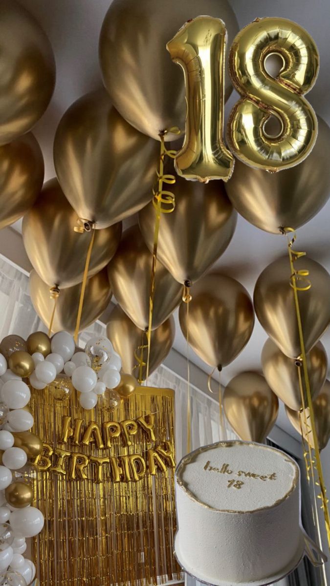 gold balloons are hanging from the ceiling in front of a birthday cake and other decorations