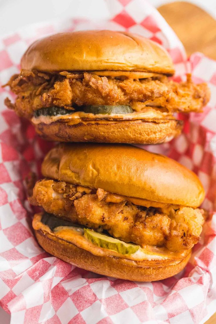 two chicken sandwiches sitting on top of a red and white checkered tablecloth covered basket