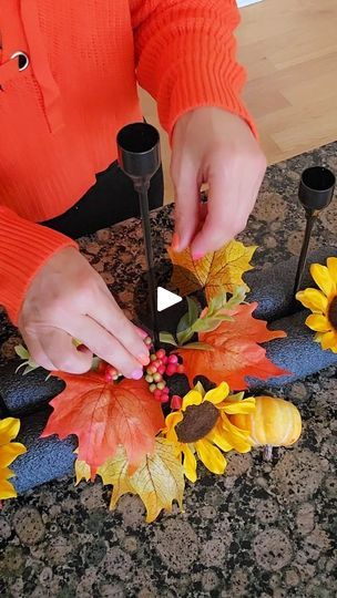 a woman in an orange sweater is decorating some fake sunflowers and leaves