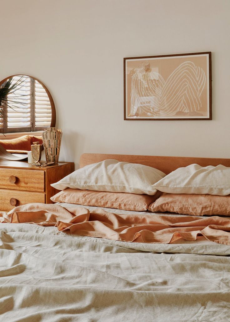 an unmade bed with white sheets and pillows in front of a round mirror on the wall