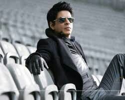 a man sitting on the bleachers at a stadium wearing sunglasses and a black jacket