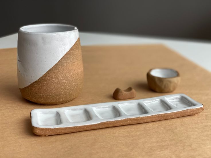 a white and brown vase sitting on top of a wooden table next to a cup