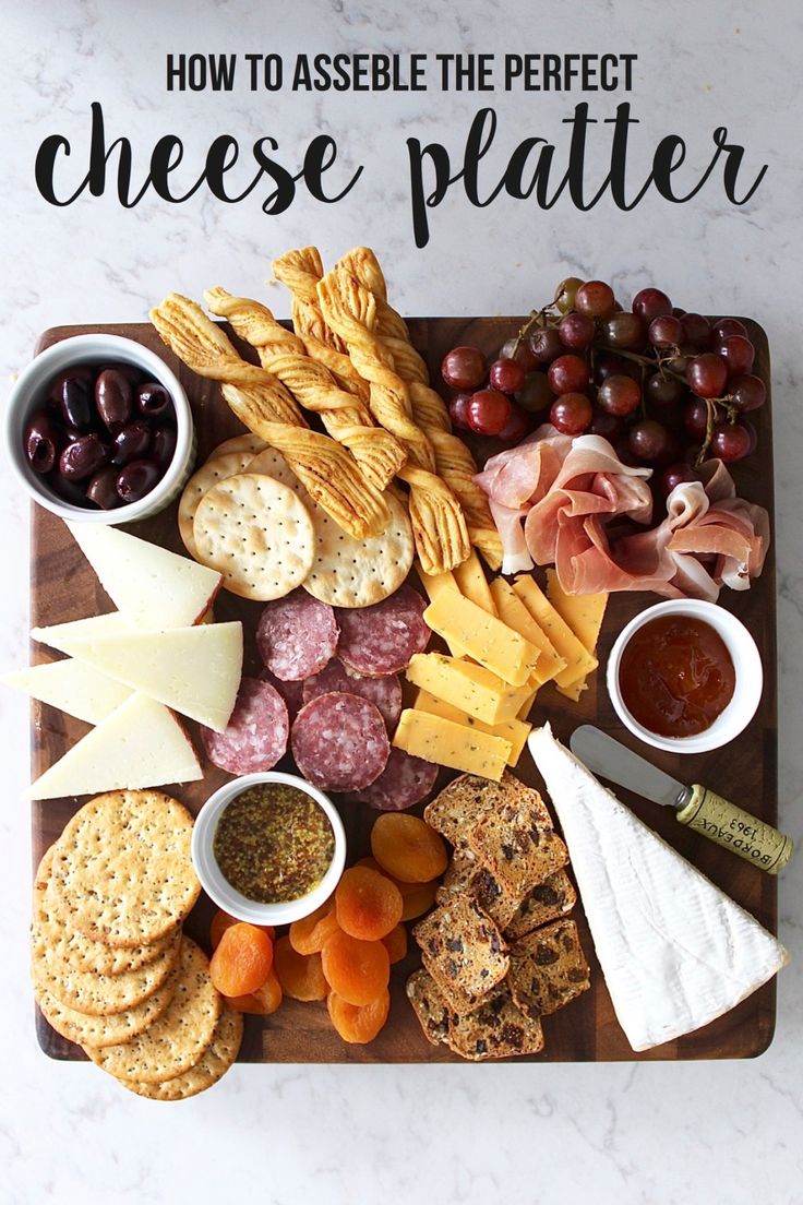 a cheese platter with crackers, olives, grapes, and meats