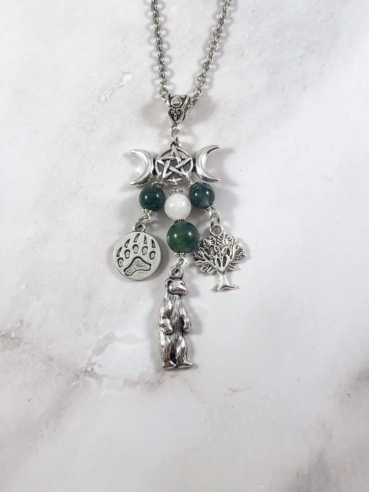 This beautiful chain necklace is the perfect way to express your affinity for the Celtic goddess Artio. Charms: Bear Claw Bear Tree 3 moss agate beads and one moonstone bead also make up the pendant. Your choice of top charm: Pentacle, Chandelier, Triple Moon, or Celtic Knot Available in a variety of lengths. Secured with a lobster clasp. Chain is stainless steel. Charms are zinc alloy. All materials are lead and nickel free. Comes in a jewelry box so it's ready to be given as a gift. Have a ide Silver Dangle Charm Necklace With Natural Stones, Spiritual Moon Charm Necklaces For Healing, Spiritual Healing Moon Charm Necklaces, Handmade Moonstone Dangle Necklace, Spiritual Agate Dangle Necklaces, Spiritual Dangle Necklaces With Moon Charm, Spiritual Crystal Pendant Necklace With Charms, Silver Charm Necklace With Natural Stones For Healing, Handmade Silver Charm Necklace For Wellness