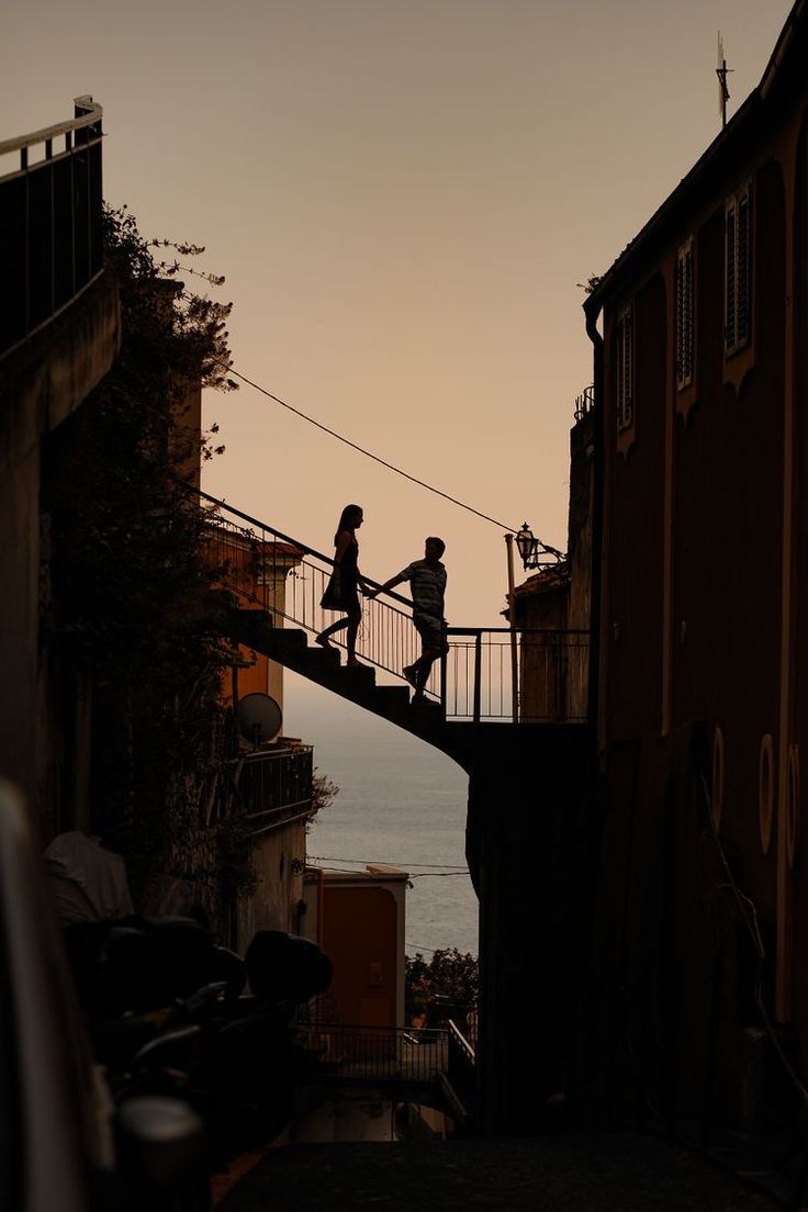 two people walking across a bridge over water at sunset or dawn with the sun setting in the background