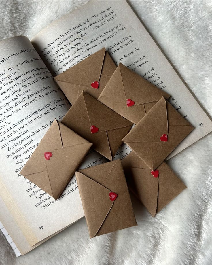 some brown envelopes with red hearts are on top of an open book