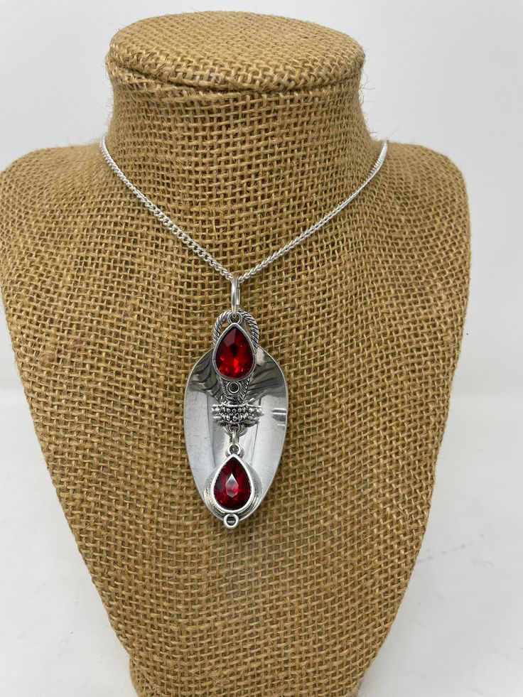 a necklace on a mannequin wearing a silver pendant with two red glass tears