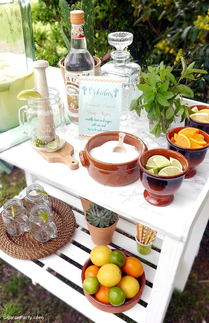 an outdoor table with drinks and fruit on it, including lemons, oranges, limeade