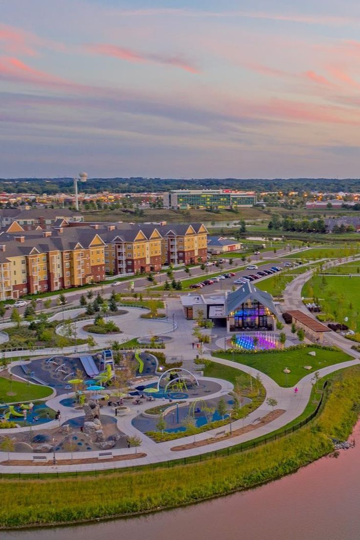 an aerial view of a park with water and playgrounds in the background at sunset