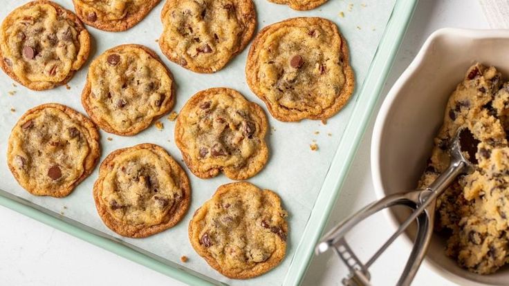 chocolate chip cookies on a baking sheet with a bowl of oatmeal in the background