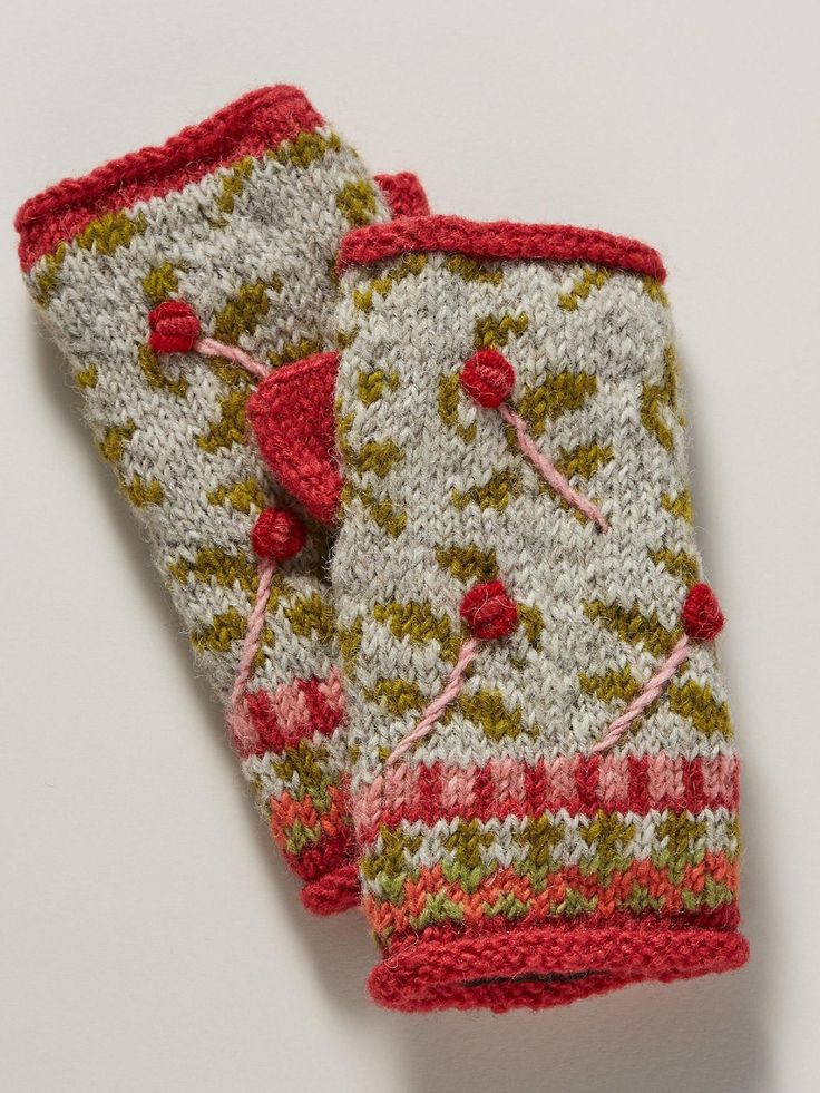 two knitted mittens sitting next to each other on a white surface with red and green designs