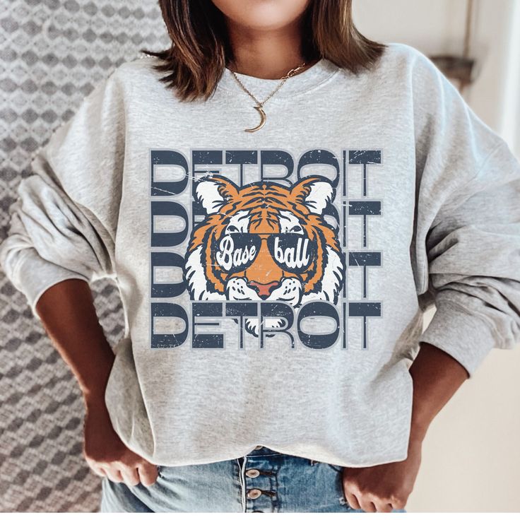 This Detroit Baseball Sweatshirt is the perfect game day apparel. Show your Tigers Baseball pride with this fun retro inspired Detroit crewneck. If you are a Tigers fan then this cozy sweatshirt is a must have to add to your collection. This is a looser fit sweatshirt, but true to size. We recommend sizing up 2 sizes if you want a trendy oversized look. - M A T E R I A L S - Gildan® Sweatshirt 8 oz./yd² (US) 50/50 cotton/polyester Heather Sport colors: 60/40 polyester/cotton Loose Fit Ribbed Knit Collar to retain shape - C A R E  I N S T R U C T I O N S - Inside out, wash with delicate cycle Do not iron directly onto the design Do not bleach Do not dry clean. - M A T E R I A L S - Gildan® Sweatshirt 8 oz./yd² (US) 50/50 cotton/polyester Heather Sport colors: 60/40 polyester/cotton Loose Fi Varsity Sweatshirt With Graphic Print For Fans, Varsity Graphic Print Sweatshirt For Fan Gear, Baseball Season Sweatshirt With Graphic Print For Fans, Sports Fan Baseball Sweatshirt With Graphic Print, Baseball Season Graphic Print Sports Fan Sweatshirt, Baseball Season Fan Apparel Sweatshirt With Graphic Print, Baseball Season Graphic Print Sweatshirt, Baseball Season Sports Fan Sweatshirt With Graphic Print, Sporty Graphic Print Sweatshirt For Baseball Season