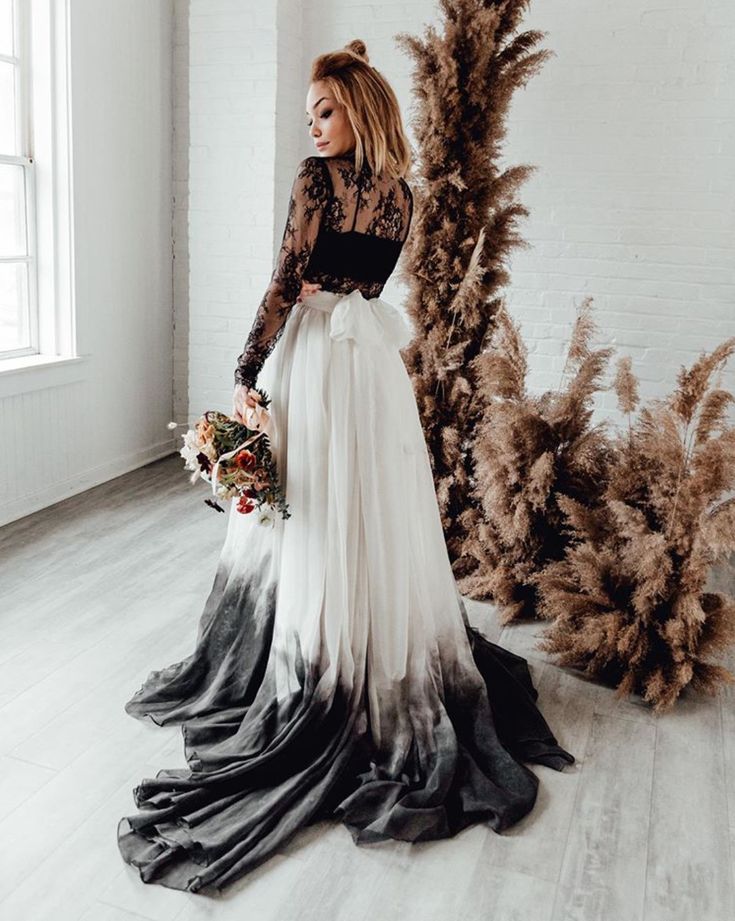 a woman is standing in front of some plants wearing a black and white wedding dress