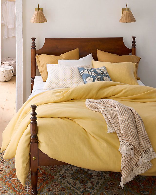 a bed with yellow linens and pillows in a white room next to two lamps