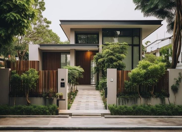 a modern house with trees and bushes in the front yard, surrounded by greenery