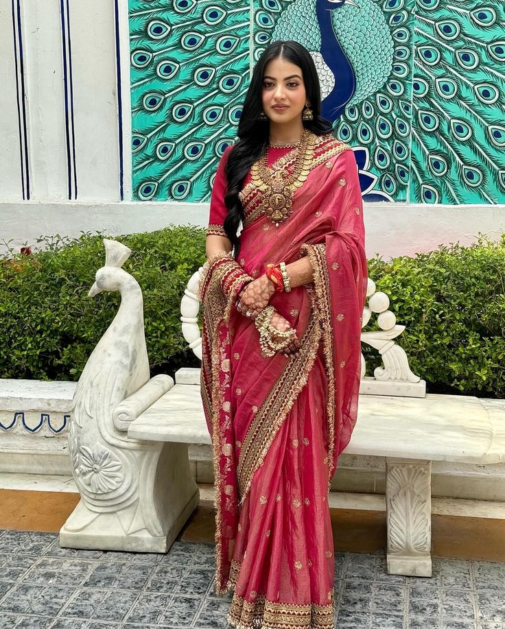 a woman in a red and gold sari standing next to a peacock wallpaper