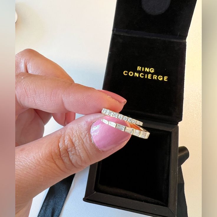 a woman's hand holding two rings in front of a black box with the word ring concier written on it