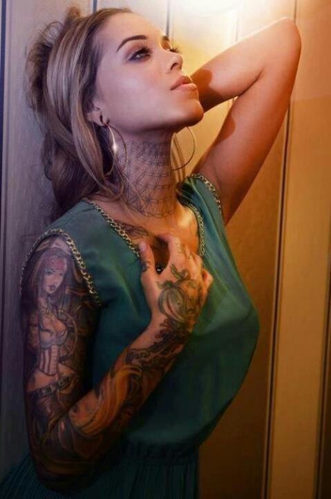 a woman with tattoos leaning against a wall