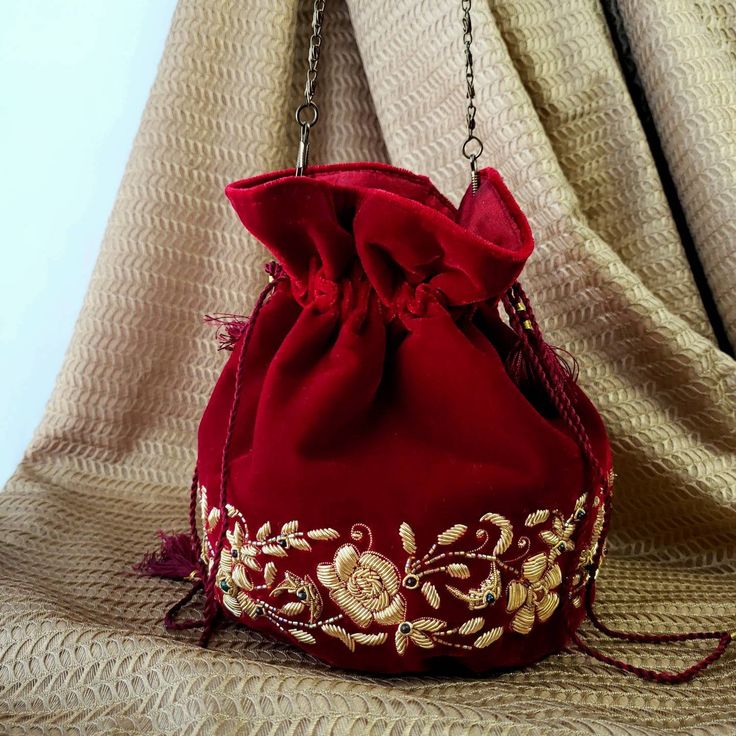 "The sweetest petite potli bag to enhance any outfit! Hand embroidered with pale gold metallic flowers on luxurious red velvet and embellished with genuine semi precious stones to create an opulent effect. It is certain to bring you compliments. Perfect for Indian weddings! Expertly hand embroidered by third generation master zardozi artisans. Of heirloom quality. - Measures approx 7\" tall, base is 4\" across. - Useable interior space is 5 x 4\". - Wrist cord with tassel, 6 in. drop - Additiona Metallic Flowers, Potli Bag, Pumpkin Patch Outfit, Wrist Bag, Embroidered Handbag, Wedding Red, Potli Bags, Wedding Purse, Handcrafted Bags