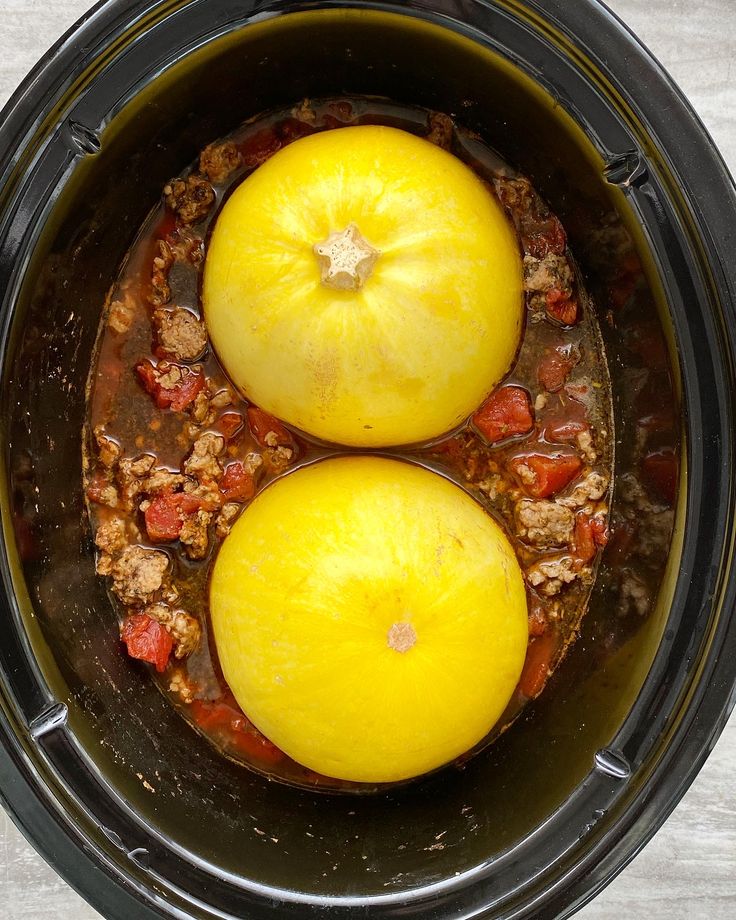 two yellow tomatoes are in the crockpot with meat and sauce on top, ready to be cooked