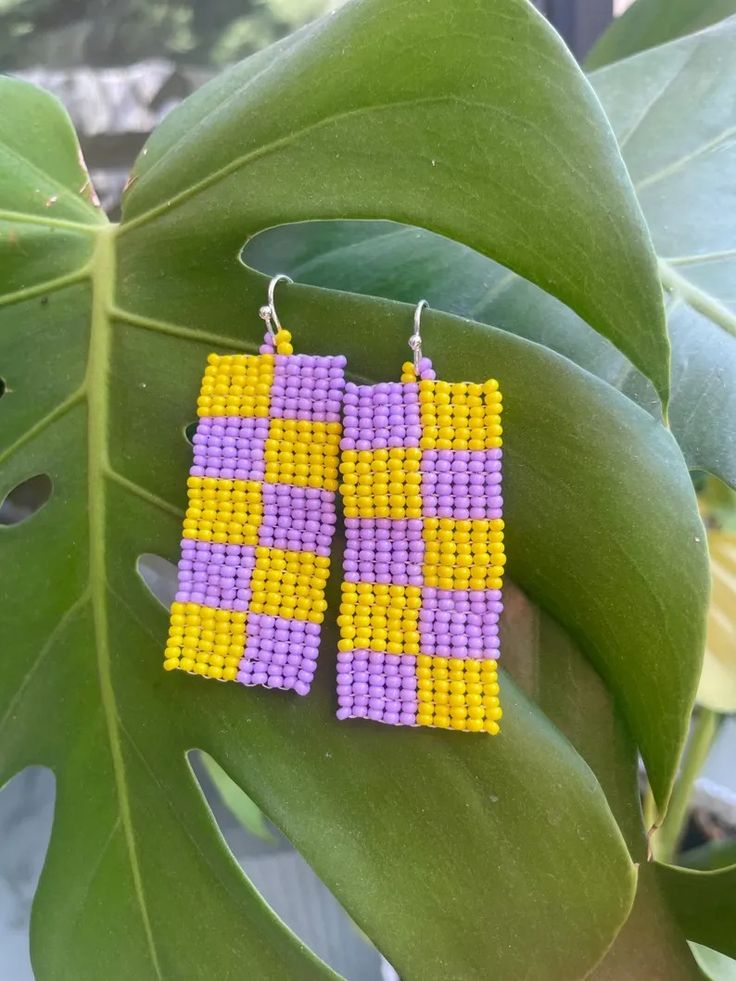 purple and yellow beaded earrings sitting on top of a green leaf