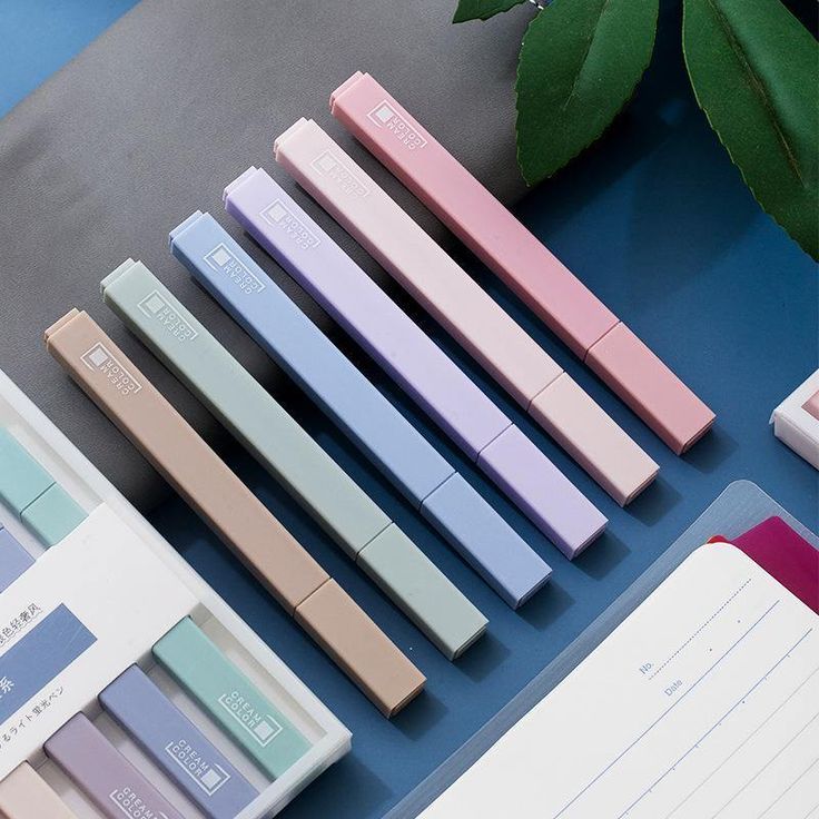 several different colored pens sitting next to each other on a blue surface with a plant in the background