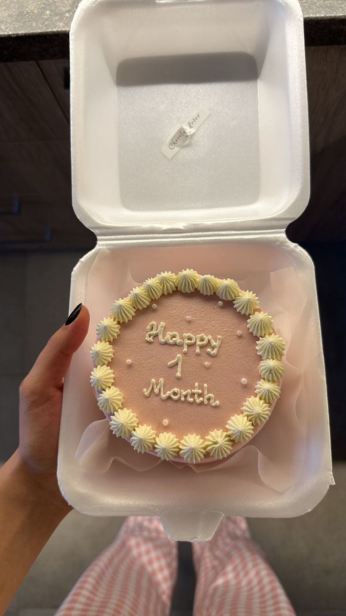 a person holding up a cake in a box with the words happy 1 month written on it