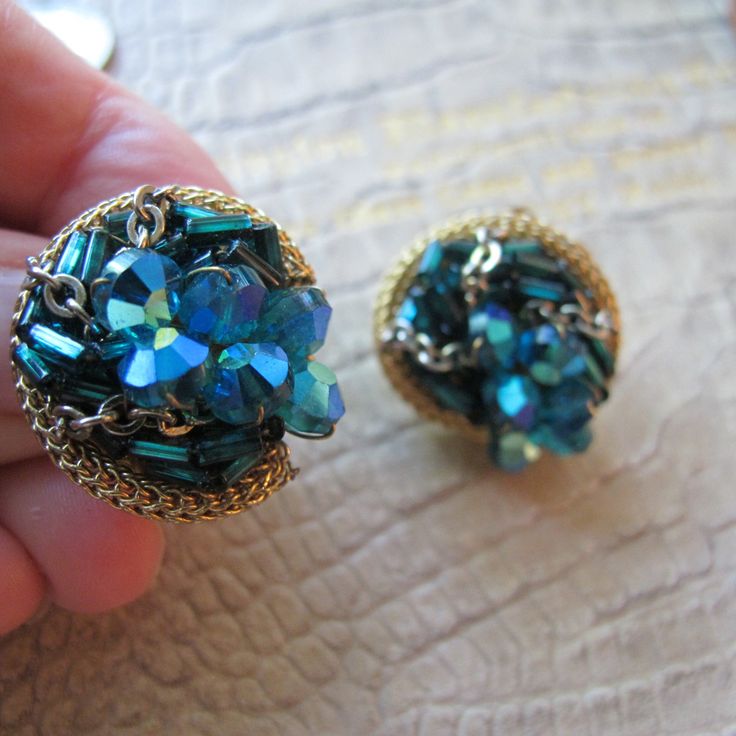 Designer Style Peacock AB Crystal Bead Cluster & Gold Tone Chains Clip Back Earrings. Signed "Pat Pend" Clip Earrings, Designer Look Quality and likely made. The bead are 3 styles in blues, hints of green, and bugles are darker teal green blue. The beads are hand wire wrapped and overall cluster epoxy adhered to the filigree floret backing.  7/8 IN to 15/16 IN roundish  Pat Pend Stamped on clips  Clips  Late 1950's to 1960's In the style of Alice Caviness to Vendome to various other fashion jewe Dark Teal, Clip Earrings, Designer Style, Teal Green, Crystal Beads, Clip On Earrings, Wire Wrapped, Gold Tones, Jewelry Earrings