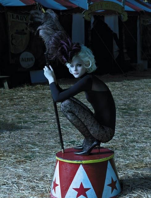 a woman sitting on top of a barrel with a feather in her hand and holding onto a pole