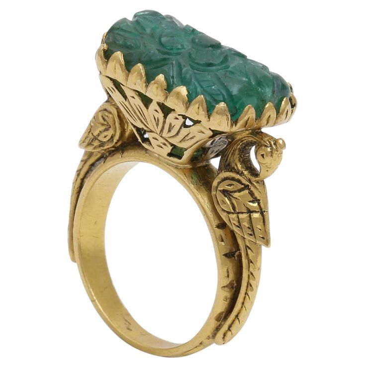 A Beautifully hand Carved Zambian Emerald set in a hand made 22K Gold Ring. The ring has intricate gold work and right below the stone are 2 magnificent peacocks holding the stone. The carved stone is inspired from the Mughal times when the Mughal rulers loved carvings on Gemstone. The national bird of India is a peacock which gave us inspiration to delicately make that on Gold. All around the stone is really intricate work done on the cocktail ring by our highly trained artisans who took long t Luxury Traditional Carved Rings, Luxury Carved Jewelry For Formal Occasions, Art Deco Carved Collectible Jewelry, Collectible Art Deco Carved Jewelry, Heirloom Yellow Gold Engraved Emerald Ring, Luxury Green Intaglio Rings, Heirloom Engraved Emerald Ring In Yellow Gold, Antique Yellow Gold Emerald Ring, Ceremonial Yellow Gold Emerald Heirloom Ring