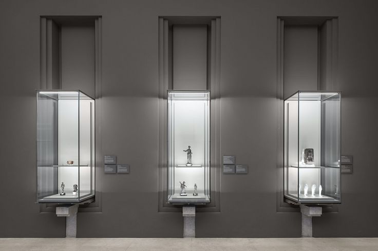 three urinals with glass cases on the wall in a room that looks like it is empty